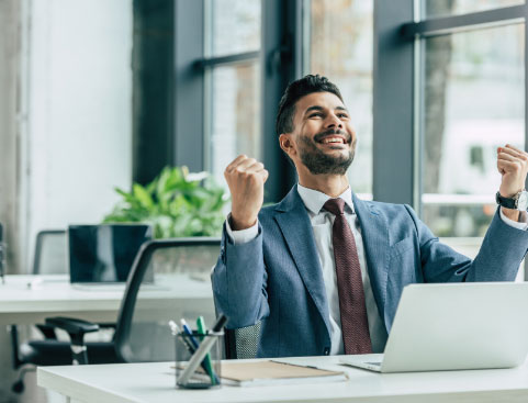 Excited businessman sitting at his desk in front of his laptop