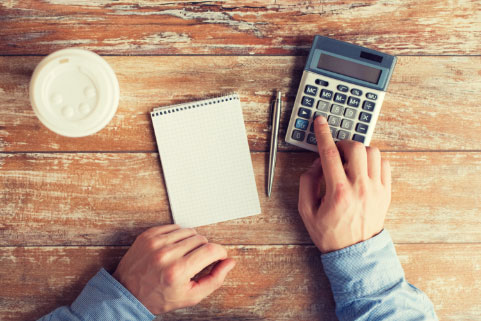Shot of calculator, notepad, pen, and coffee on a wooden table