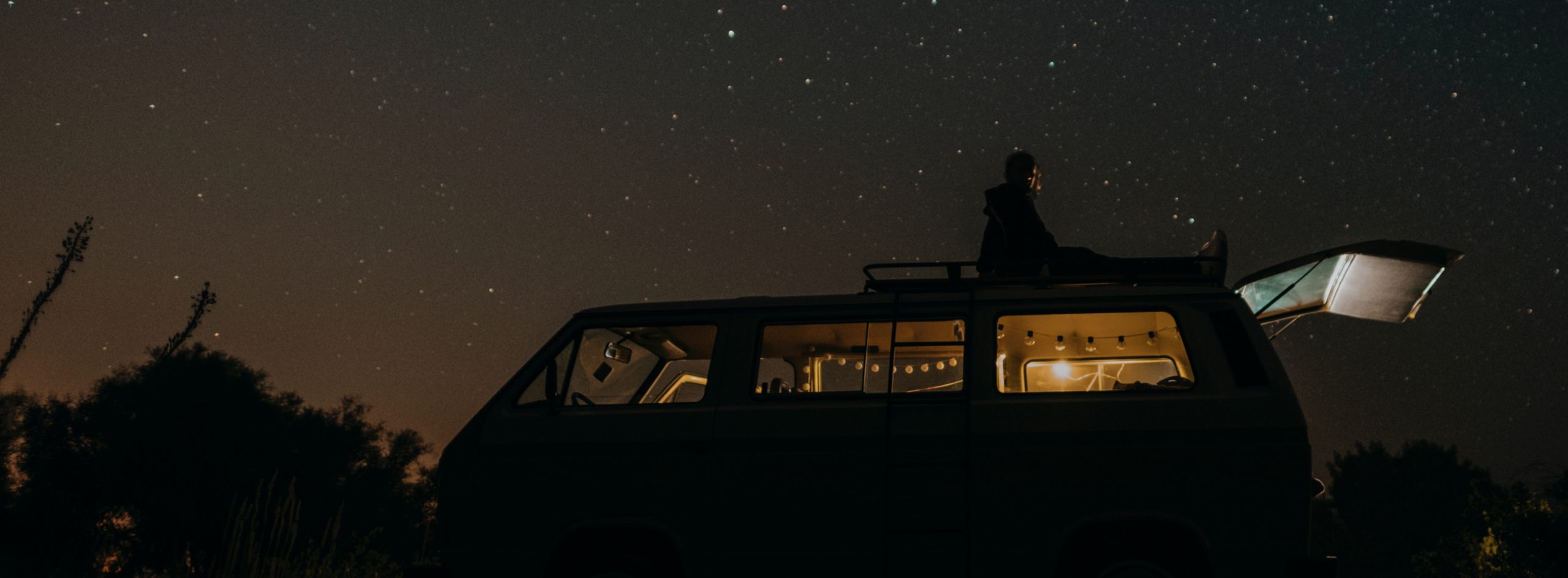Man sitting on top of an RV under the stars